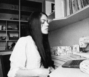 Rita Apoena, de perfil, escrevendo em um notebook.